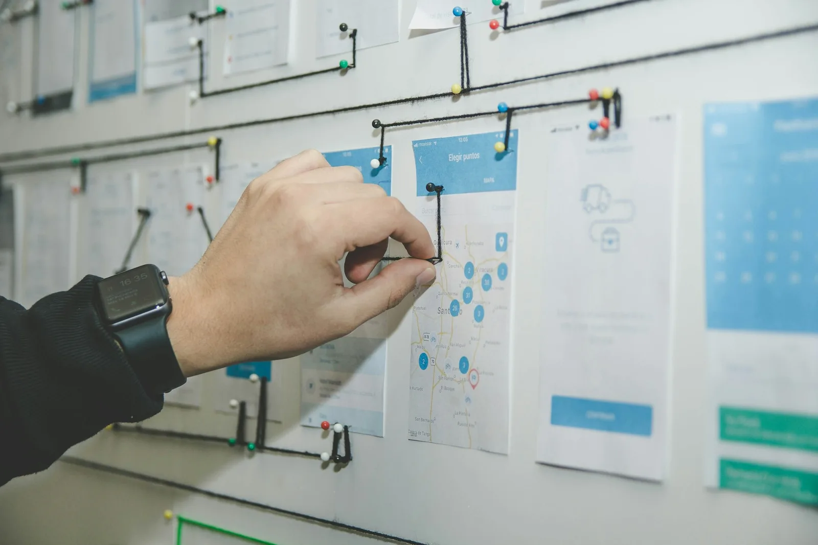 App screens pinned to a wall and connected with thread, mapping a product journey